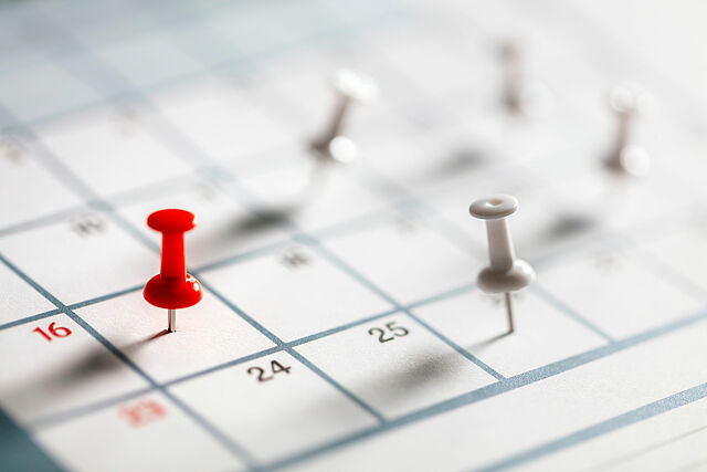 Auf einem Kalender markieren einzelne Pinnwandnadeln bestimmte Tage.
