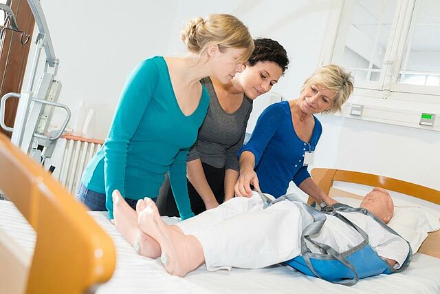 Eine Praxisanleiterin zeigt den Umfang mit Patienten im Pflegebett.